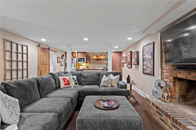 living room with a brick fireplace, a barn door, and dark hardwood / wood-style floors