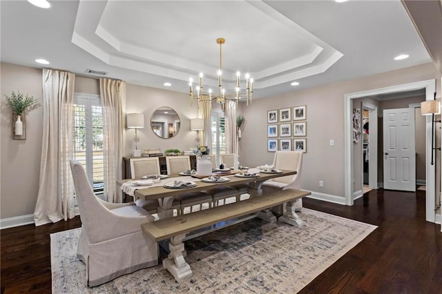 dining area featuring dark wood-type flooring, a tray ceiling, and a chandelier