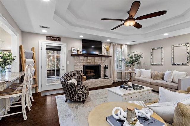 living room featuring ceiling fan, dark hardwood / wood-style flooring, a raised ceiling, and a fireplace