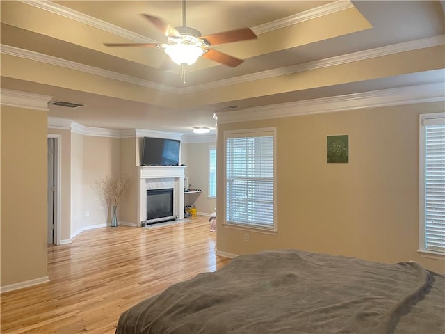 bedroom with visible vents, a premium fireplace, crown molding, light wood-style floors, and a raised ceiling