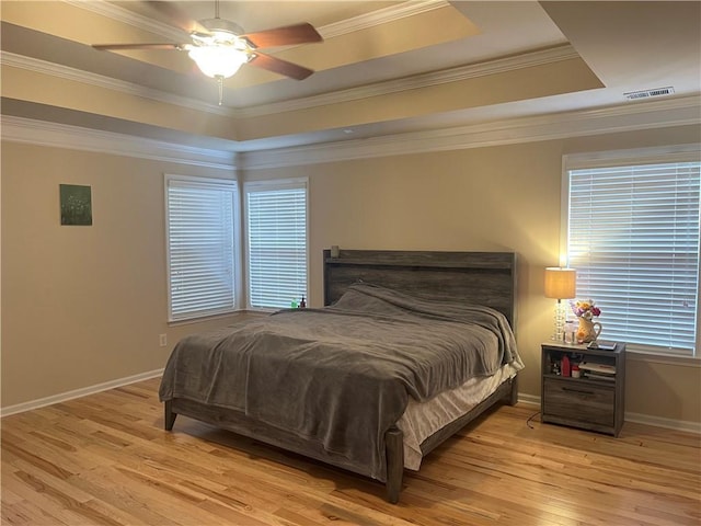 bedroom with visible vents, light wood-type flooring, a raised ceiling, and baseboards