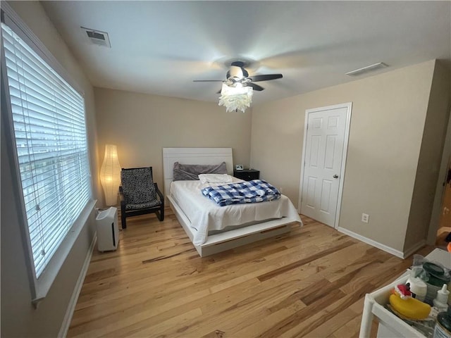 bedroom featuring a ceiling fan, light wood-style floors, visible vents, and baseboards