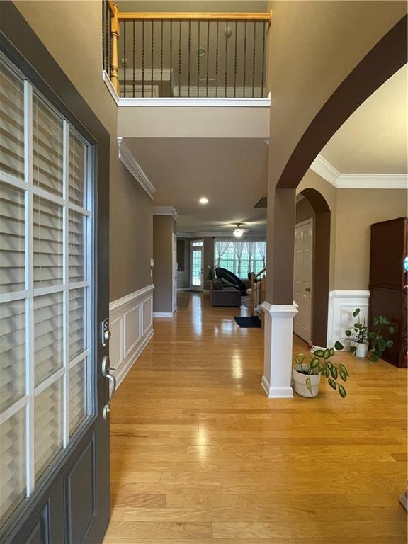 entryway featuring a wainscoted wall, ornamental molding, light wood-style floors, arched walkways, and a decorative wall