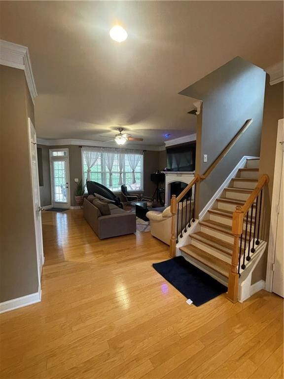 living area with stairway, light wood-style flooring, a fireplace, and ornamental molding