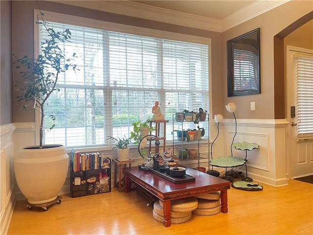 sitting room with a wainscoted wall, wood finished floors, ornamental molding, and a decorative wall