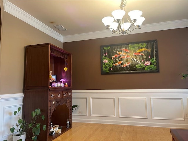 dining area with wood finished floors, a wainscoted wall, visible vents, ornamental molding, and a chandelier