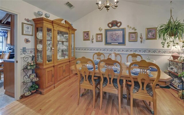 dining room with a wainscoted wall, vaulted ceiling, a chandelier, visible vents, and light wood-style floors