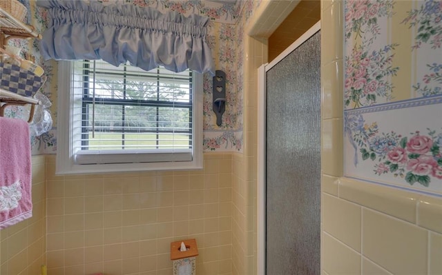 bathroom with a stall shower, wainscoting, wallpapered walls, and tile walls