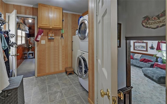 laundry area with tile patterned flooring, crown molding, wood walls, stacked washing maching and dryer, and laundry area