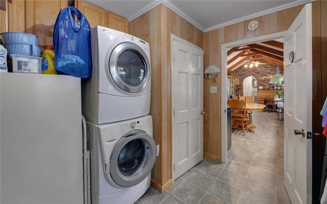 laundry area featuring wooden walls, stacked washer and clothes dryer, laundry area, and ornamental molding