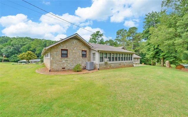 rear view of property featuring a lawn, stone siding, and central AC