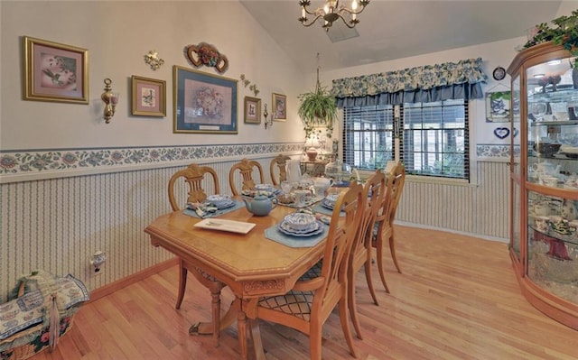 dining area featuring lofted ceiling, a notable chandelier, wallpapered walls, and wainscoting