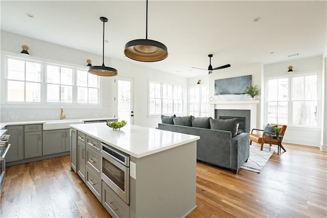 kitchen featuring sink, a center island, light hardwood / wood-style flooring, stainless steel microwave, and pendant lighting