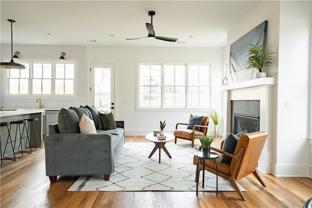 living room featuring ceiling fan, a healthy amount of sunlight, light hardwood / wood-style floors, and a tile fireplace