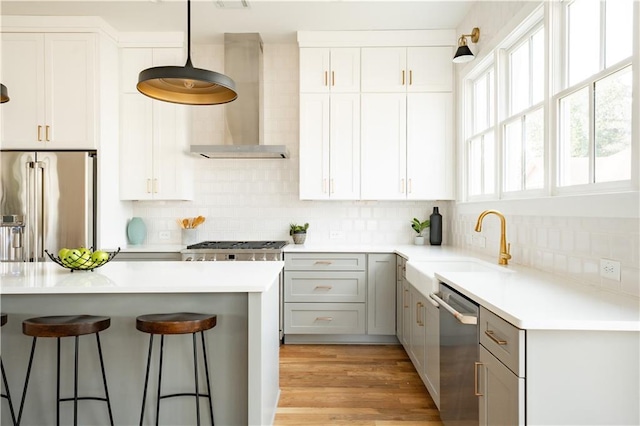 kitchen featuring gray cabinets, appliances with stainless steel finishes, pendant lighting, sink, and wall chimney exhaust hood