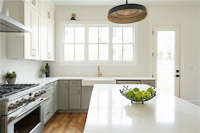 kitchen with appliances with stainless steel finishes, decorative light fixtures, sink, backsplash, and wall chimney range hood