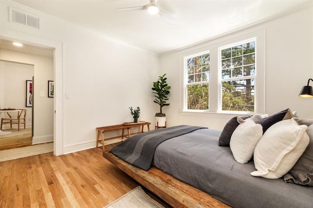 bedroom featuring light wood-type flooring, visible vents, ornamental molding, a ceiling fan, and baseboards