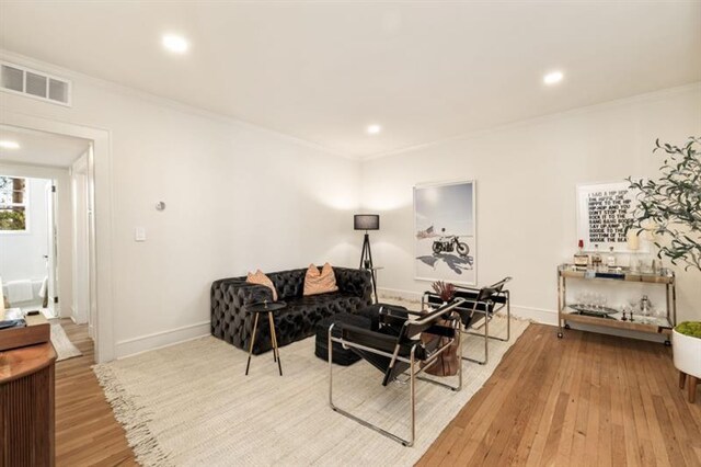 living room featuring wood finished floors, baseboards, visible vents, recessed lighting, and ornamental molding