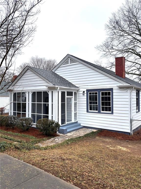 rear view of property featuring a shingled roof, a chimney, and a sunroom