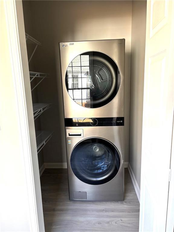 clothes washing area featuring baseboards, stacked washing maching and dryer, and wood finished floors