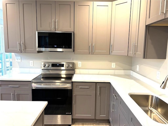 kitchen with stainless steel appliances, gray cabinets, light countertops, and a sink