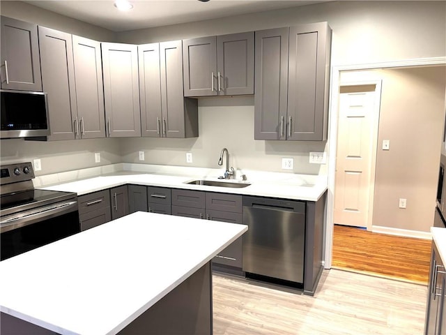 kitchen with appliances with stainless steel finishes, light countertops, gray cabinetry, light wood-type flooring, and a sink