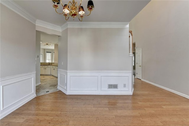 interior space featuring a chandelier, visible vents, wainscoting, light wood finished floors, and crown molding