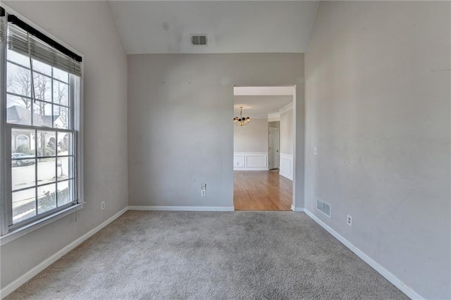 carpeted empty room featuring baseboards, vaulted ceiling, visible vents, and a chandelier