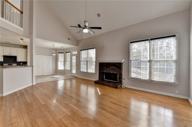 unfurnished living room featuring a fireplace, light wood-style flooring, a ceiling fan, high vaulted ceiling, and baseboards