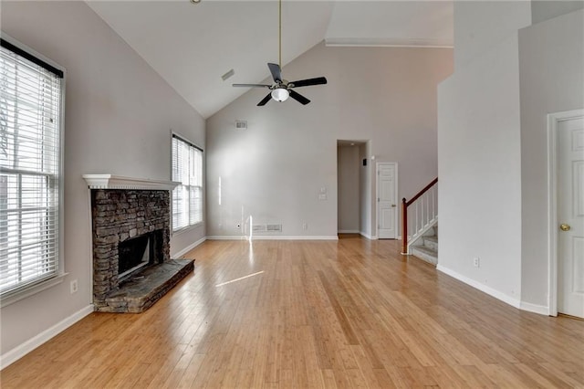 unfurnished living room featuring light wood finished floors, ceiling fan, a stone fireplace, baseboards, and stairs