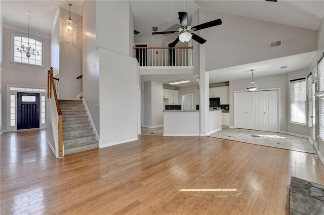 unfurnished living room featuring light wood finished floors, baseboards, visible vents, stairway, and ceiling fan with notable chandelier