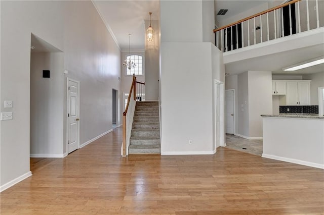 unfurnished living room with baseboards, light wood finished floors, a high ceiling, and a notable chandelier