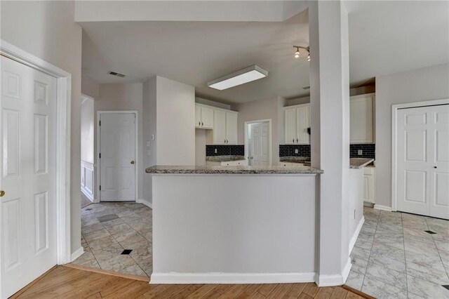 kitchen featuring light stone counters, visible vents, decorative backsplash, white cabinetry, and baseboards