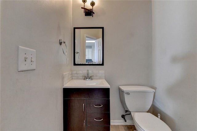 half bathroom featuring toilet, baseboards, and vanity