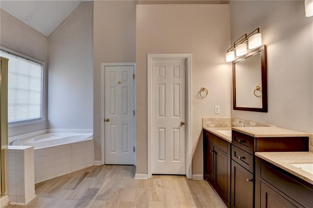 bathroom with a garden tub, vaulted ceiling, wood finished floors, and vanity