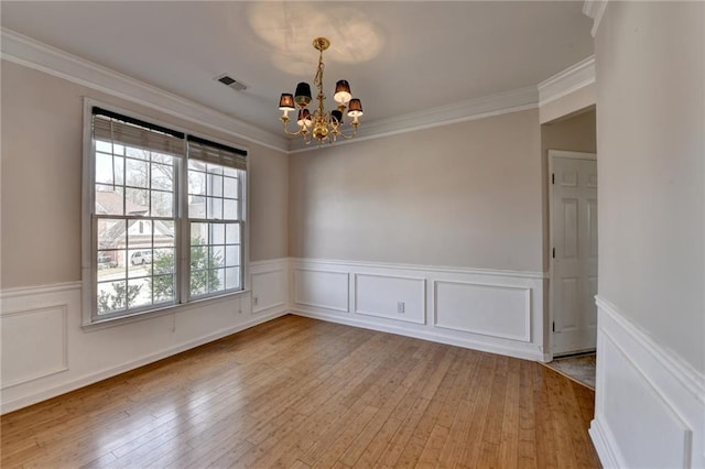 spare room with ornamental molding, light wood-type flooring, visible vents, and an inviting chandelier