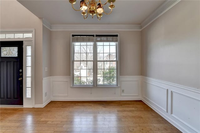 entrance foyer with hardwood / wood-style flooring, a chandelier, crown molding, and wainscoting