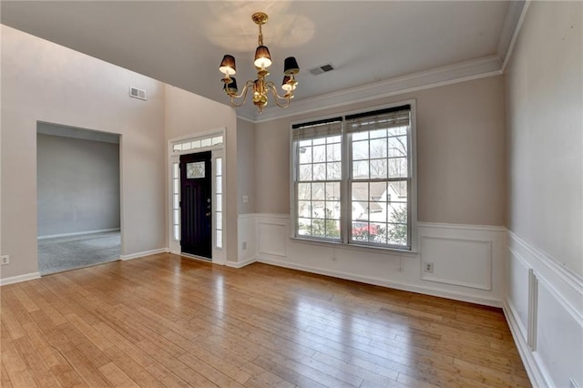 entrance foyer featuring hardwood / wood-style flooring, visible vents, wainscoting, an inviting chandelier, and crown molding