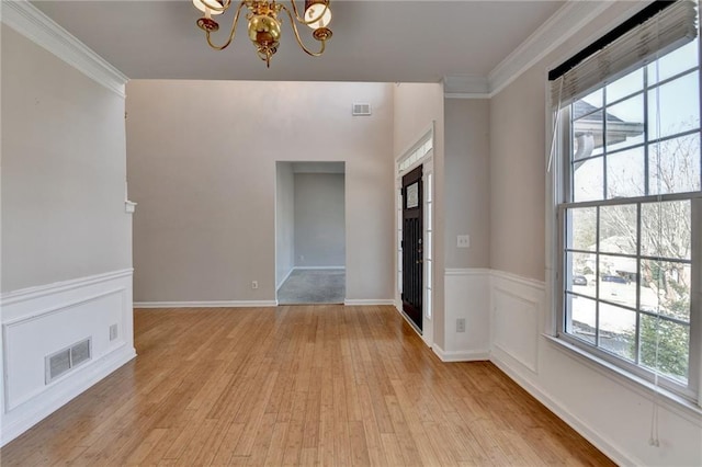 spare room featuring crown molding, light wood-style floors, visible vents, and an inviting chandelier