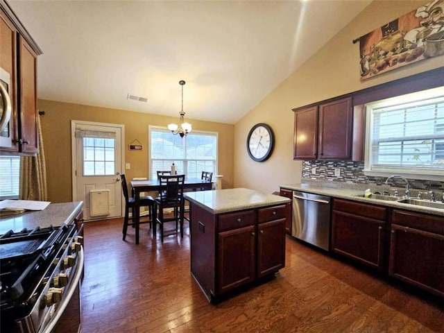 kitchen featuring dark hardwood / wood-style flooring, vaulted ceiling, a kitchen island, pendant lighting, and appliances with stainless steel finishes