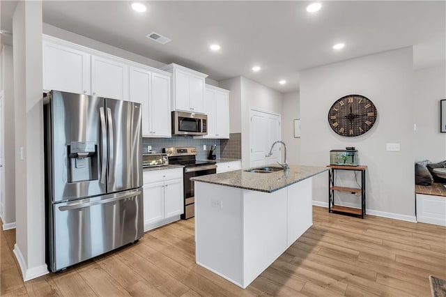 kitchen with appliances with stainless steel finishes, white cabinets, a sink, dark stone countertops, and an island with sink