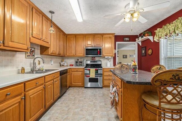 kitchen featuring a kitchen breakfast bar, a textured ceiling, stainless steel appliances, ceiling fan, and sink