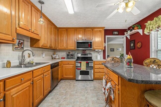 kitchen with ceiling fan, sink, stainless steel appliances, backsplash, and a kitchen bar