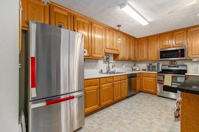 kitchen with a textured ceiling, sink, stainless steel appliances, and hanging light fixtures