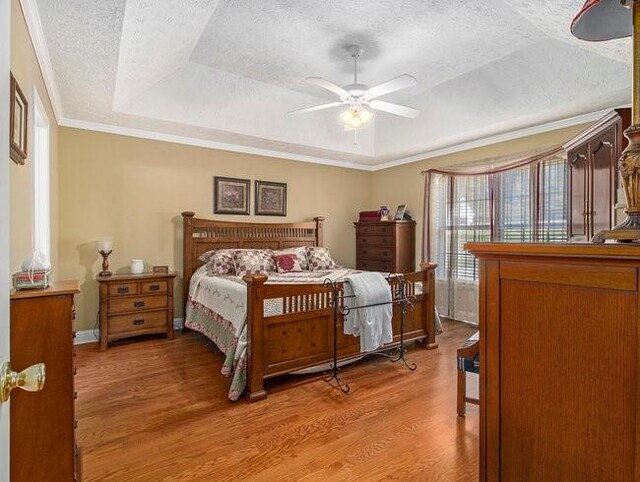 bedroom featuring a raised ceiling, crown molding, ceiling fan, a textured ceiling, and light hardwood / wood-style floors