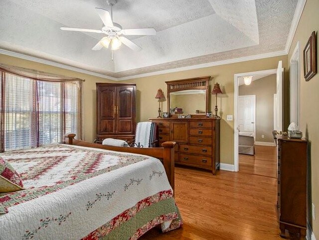 bedroom featuring hardwood / wood-style floors, ceiling fan, ornamental molding, a textured ceiling, and a tray ceiling