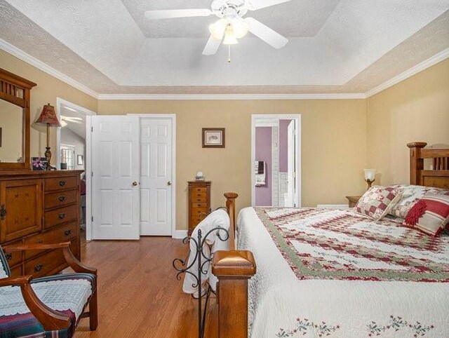 bedroom featuring ceiling fan, light hardwood / wood-style flooring, crown molding, a textured ceiling, and a tray ceiling