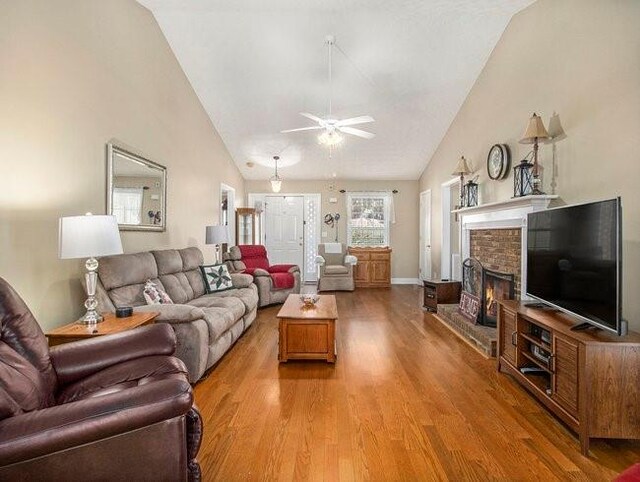 living room with ceiling fan, hardwood / wood-style floors, vaulted ceiling, and a brick fireplace