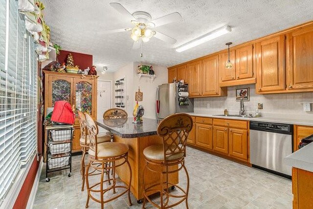 kitchen with pendant lighting, sink, ceiling fan, appliances with stainless steel finishes, and a kitchen bar