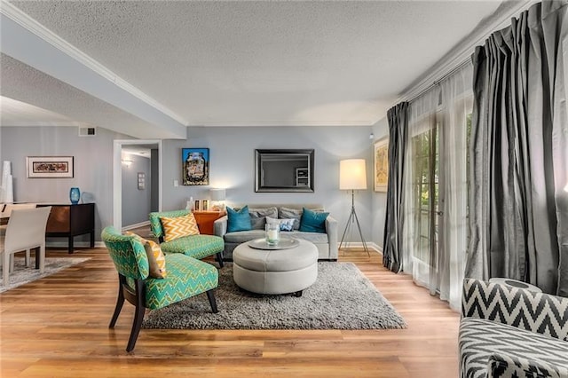 living room with light wood-style flooring, ornamental molding, baseboards, visible vents, and a textured ceiling